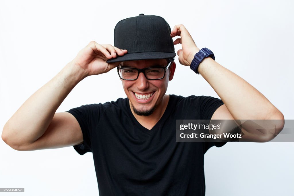 Smiling Hispanic man adjusting baseball cap