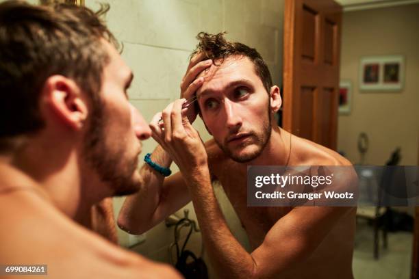 reflection of caucasian man plucking eyebrow in mirror - tweezing eyebrows stock pictures, royalty-free photos & images