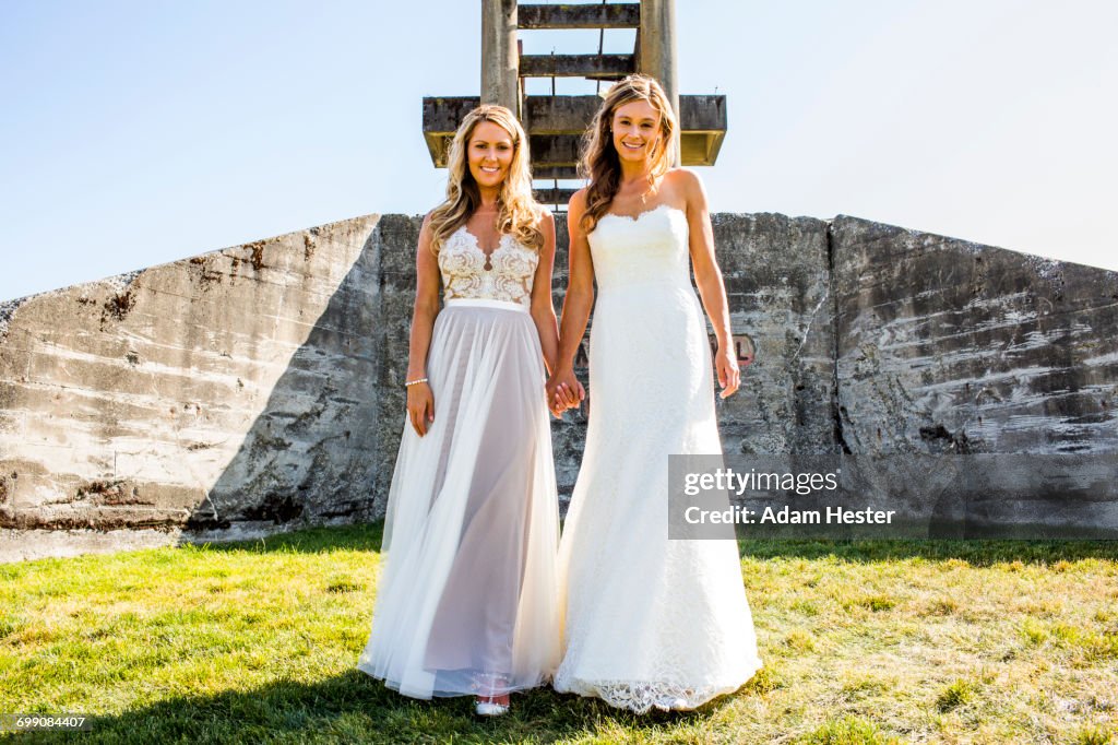 Caucasian brides holding hands in grass near concrete structure