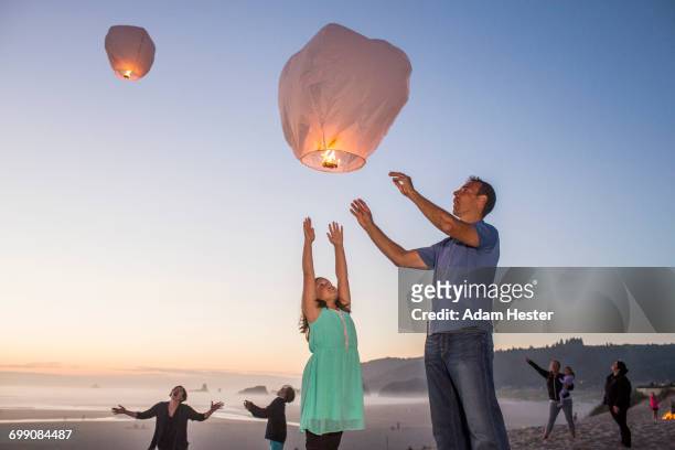 caucasian father and daughter flying lantern balloon at beach - floating lanterns stock-fotos und bilder