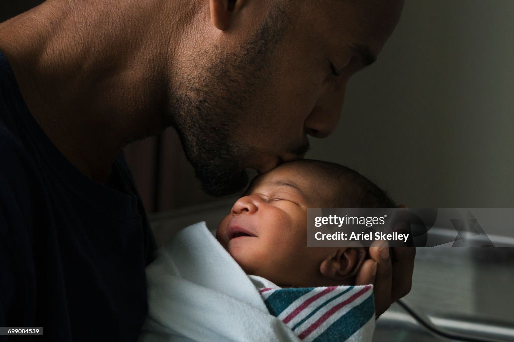 Black father kissing forehead of newborn son
