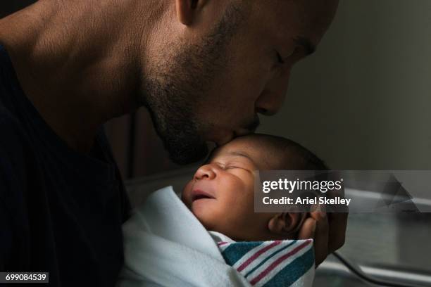 black father kissing forehead of newborn son - father holding sleeping baby stockfoto's en -beelden