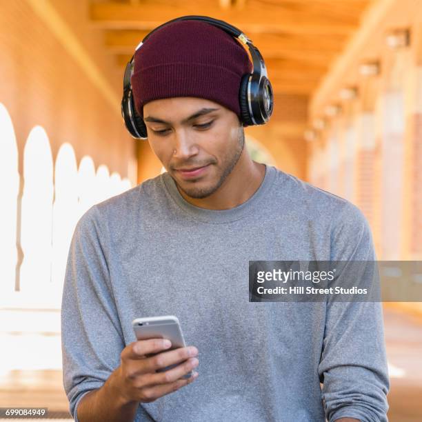 hispanic man wearing headphones texting on cell phone - interested listener stock-fotos und bilder