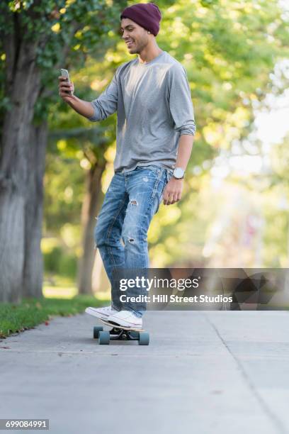 hispanic man riding skateboard and texting on cell phone - コールドウェル市 ストックフォトと画像