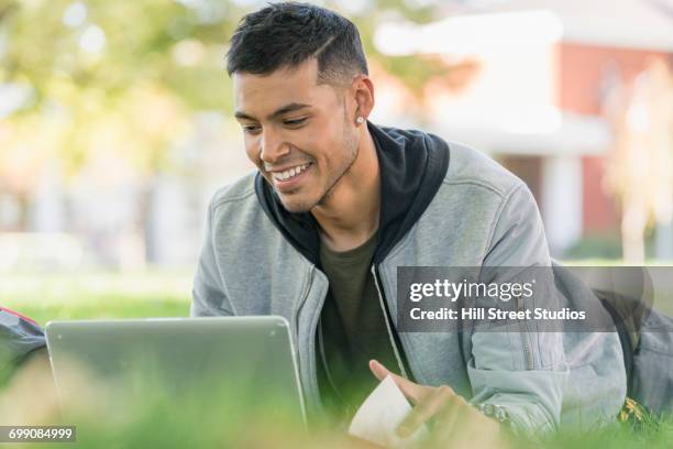 smiling hispanic man laying in grass using laptop - caldwell idaho stockfoto's en -beelden