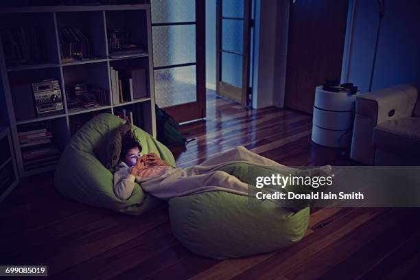 mixed race girl using cell phone laying on bean bags in dark - beanbag photos et images de collection