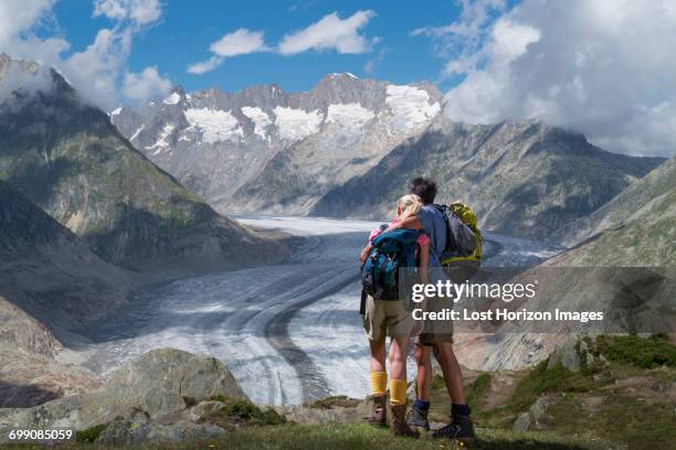 hiking couple looking out over aletsch glacier, canton wallis, switzerland - aletsch glacier stock pictures, royalty-free photos & images