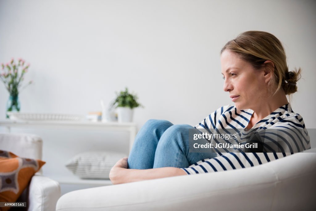 Caucasian woman sitting in armchair holding legs