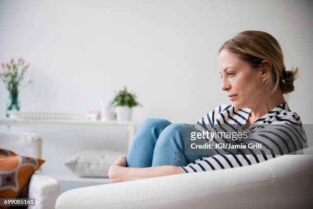 caucasian woman sitting in armchair holding legs - depression sadness stock pictures, royalty-free photos & images