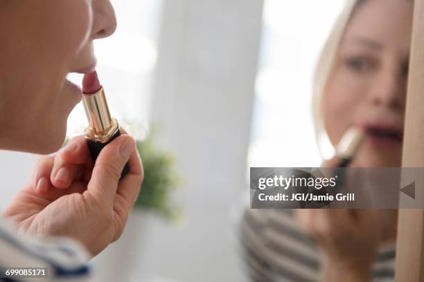 reflection of caucasian woman applying lipstick in mirror - lippenstift stock-fotos und bilder