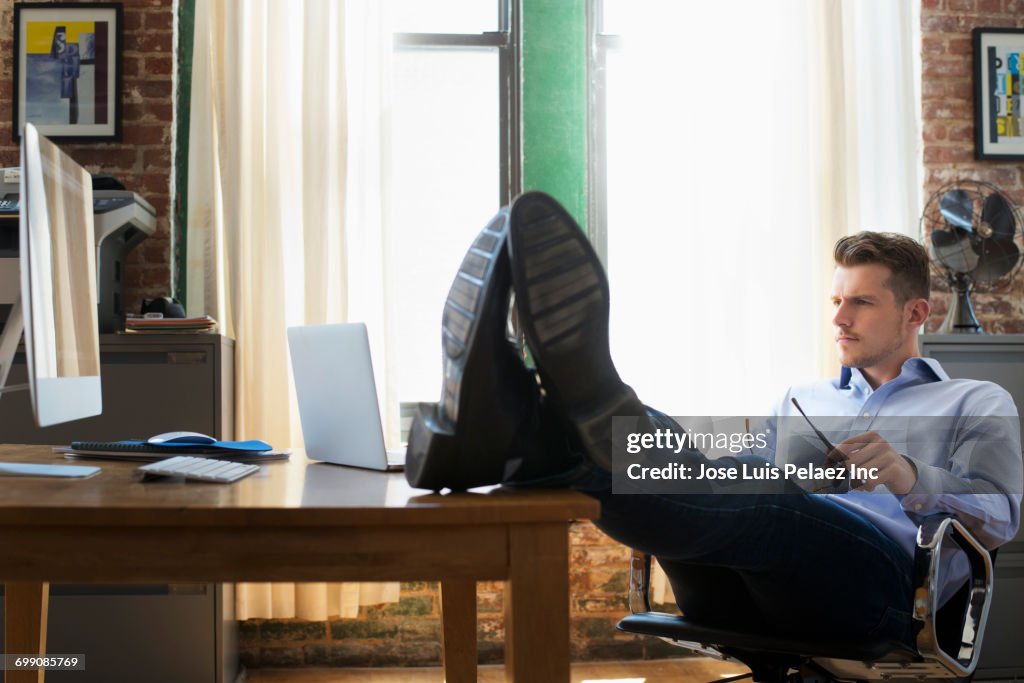 Pensive Caucasian businessman with feet up on desk