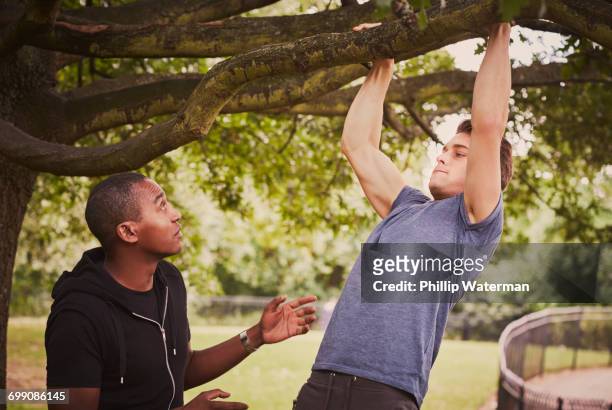 personal trainer instructing man on pull ups using park tree branch - chin ups stock pictures, royalty-free photos & images