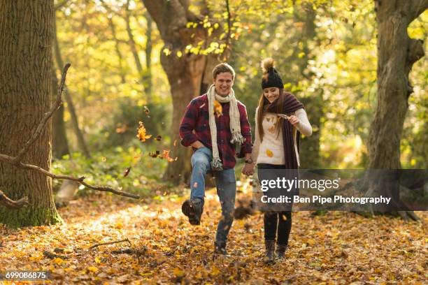 young couple walking through forest, holding hands, smiling - epping forest stock pictures, royalty-free photos & images