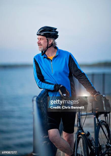 a bike commuter poses at dusk by the water. - casco protector photos et images de collection
