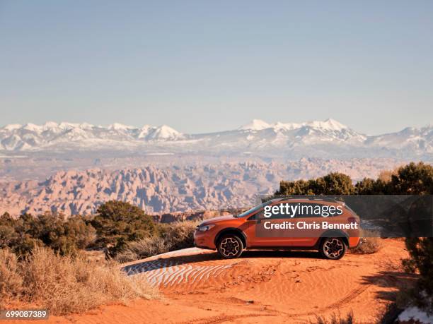 an orange car sits parked on a sand dune with the desert stretching out behind. - parked cars stock pictures, royalty-free photos & images