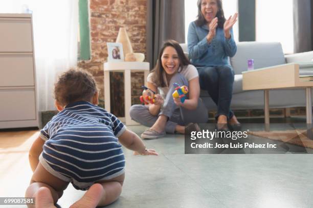 hispanic mother and grandmother watching crawling baby boy - baby crawling stock pictures, royalty-free photos & images
