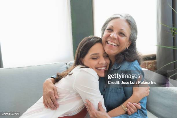hispanic mother and daughter hugging on sofa - vuxet barn bildbanksfoton och bilder