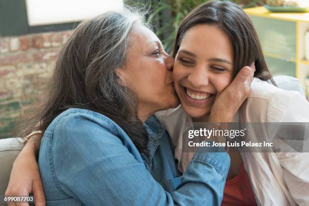 hispanic mother kissing daughter on cheek - mother and daughter kissing stock pictures, royalty-free photos & images