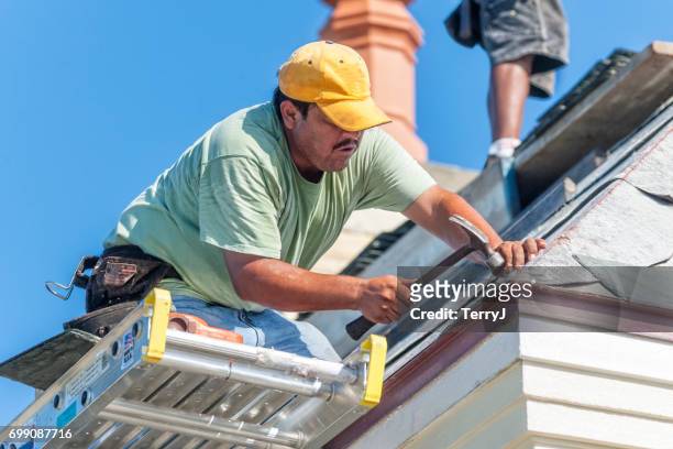 hispanic roofer hammers a copper nail into a piece of slate tile on the roof - roofing contractor stock pictures, royalty-free photos & images