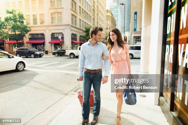 a cute young couple with their luggage walks side by side on a footpath in dallas. - side by side car stock pictures, royalty-free photos & images