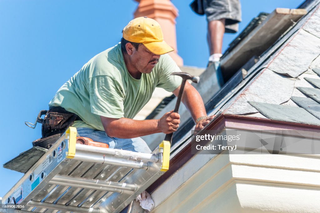 Il roofer ispanico martella un chiodo di rame in un pezzo di piastrella di ardesia sul tetto
