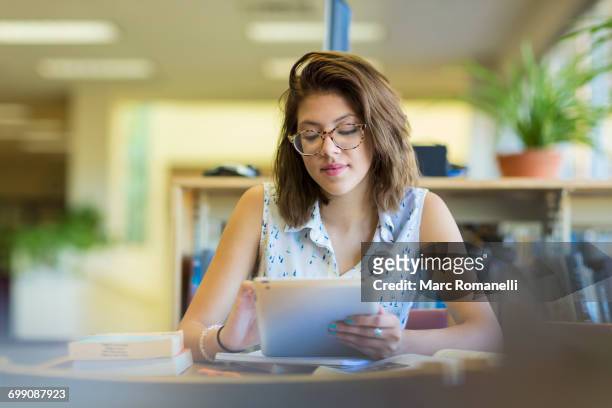 mixed race girl reading digital tablet in library - college girl pics stock-fotos und bilder