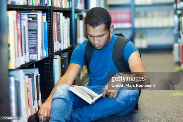 mixed race boy sitting on floor reading book in library - new mexico stock pictures, royalty-free photos & images