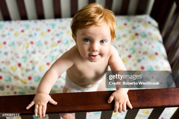 portrait of curious caucasian baby boy standing in crib - un solo niño bebé fotografías e imágenes de stock