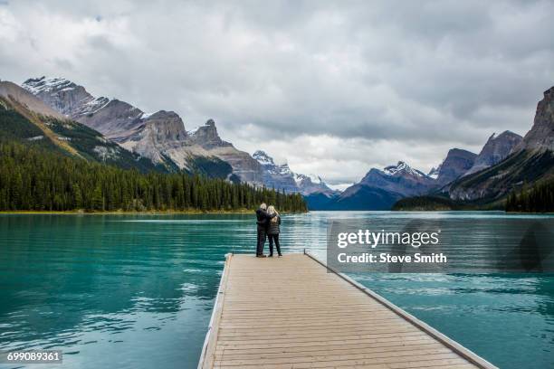 caucasian couple standing at the end of dock on mountain lake - bergsteiger stockfoto's en -beelden