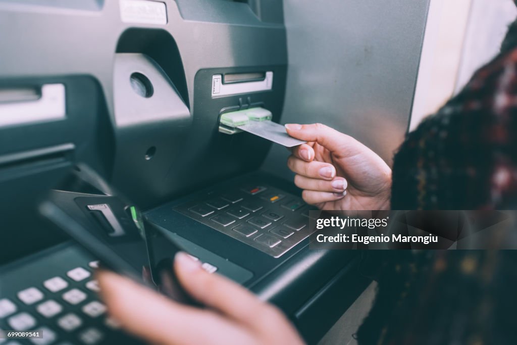 Hand of young woman inserting credit card into cash machine