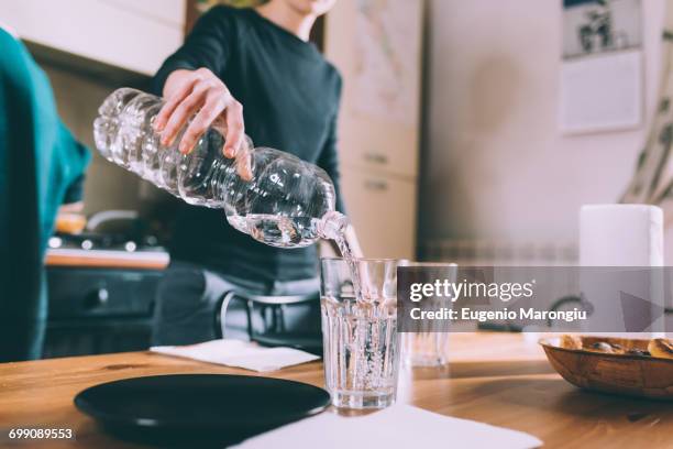 cropped shot of young woman pouring water at kitchen table - drinking glass bottle stock pictures, royalty-free photos & images