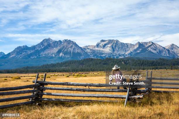 caucasian woman sitting on wooden fence near mountain river - cowgirl hairstyles stock-fotos und bilder