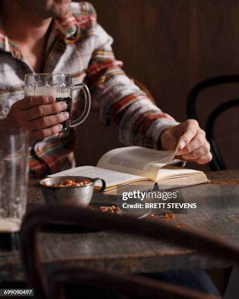 cropped shot of man drinking beer and reading book at pub table - beer nuts stock-fotos und bilder