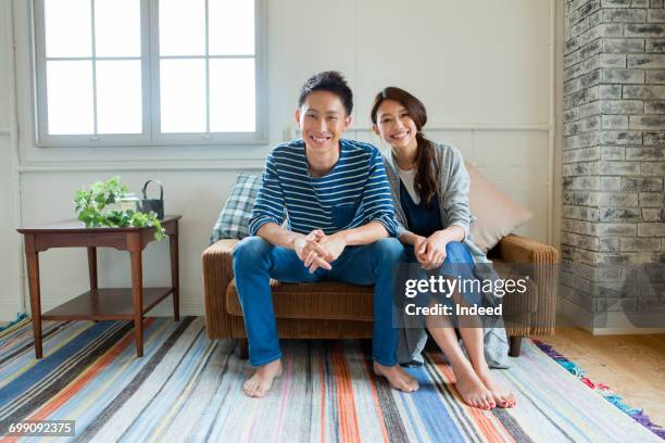 portrait of young couple, sitting on sofa - asian man barefoot foto e immagini stock