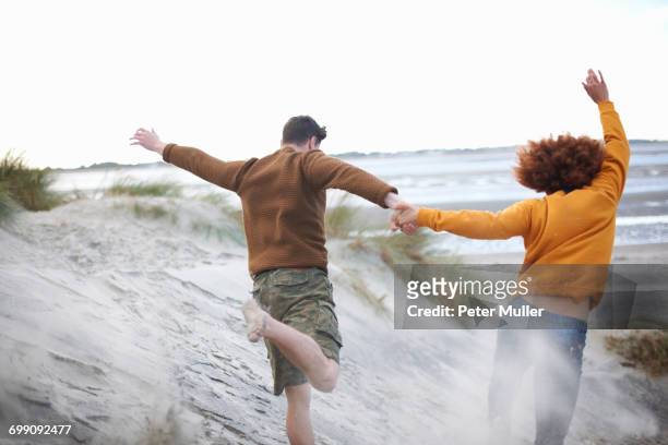 couple running down sand dunes to beach - couple dunes stockfoto's en -beelden