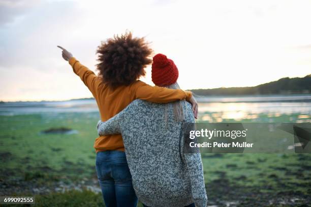 rear view of two young women by sea pointing at sunset - arms around imagens e fotografias de stock