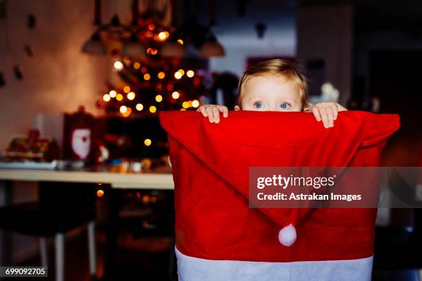 cute girl hiding behind chair covered with santa hat at home - national day celebrations in sweden 2016 imagens e fotografias de stock