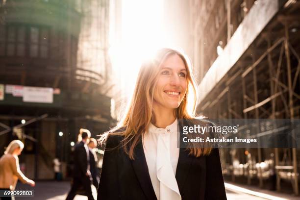 smiling businesswoman standing on city street during sunny day - formele kleding stockfoto's en -beelden