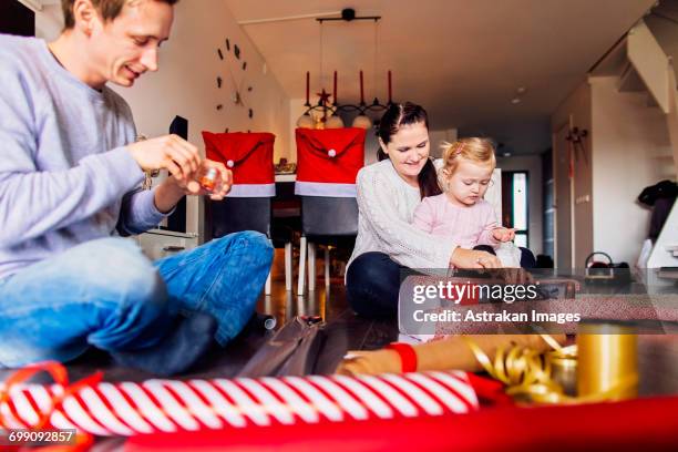 happy mother and father with daughter wrapping christmas presents at home - family with one child mother bonding family adult daughter focus on background leisure stock-fotos und bilder
