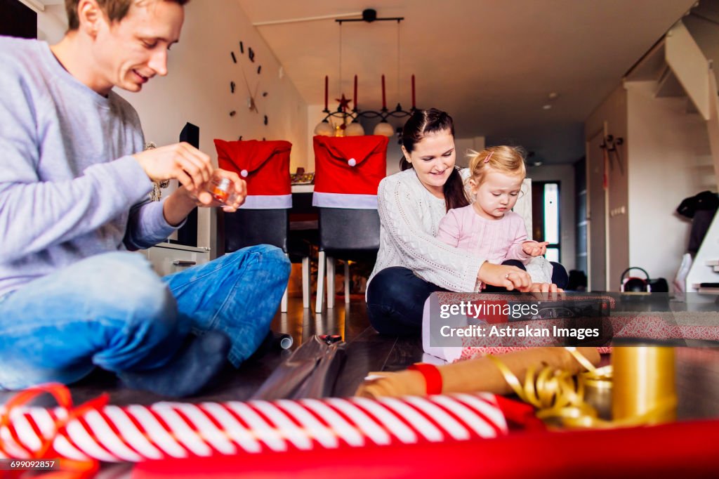 Happy mother and father with daughter wrapping Christmas presents at home