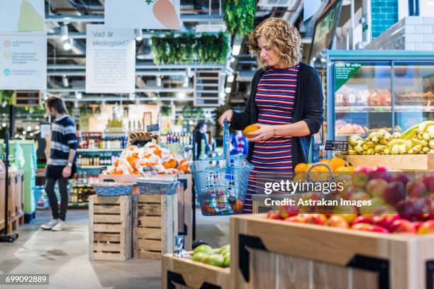 woman buying oranges while carrying shopping basket in supermarket - oranges in basket at food market stock pictures, royalty-free photos & images