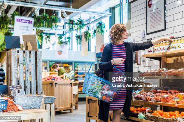 young woman buying fruit juice while carrying basket at supermarket - organic bildbanksfoton och bilder