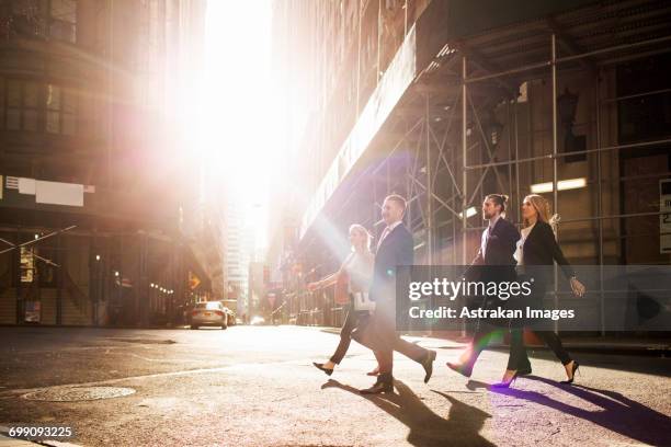 business people walking on city street by buildings during sunny day - business sunlight stock pictures, royalty-free photos & images