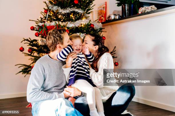 parents kissing daughter while sitting against christmas tree at home - national day celebrations in sweden 2016 imagens e fotografias de stock