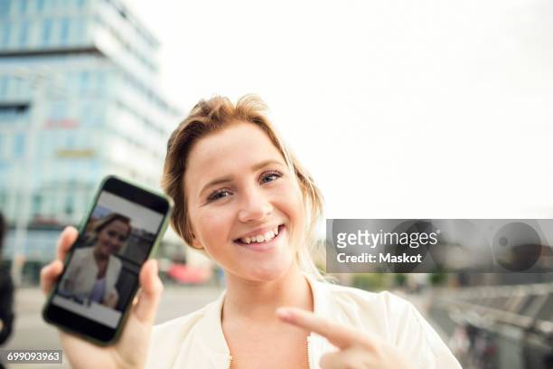 portrait of happy woman showing photograph in mobile phone - tonen stockfoto's en -beelden