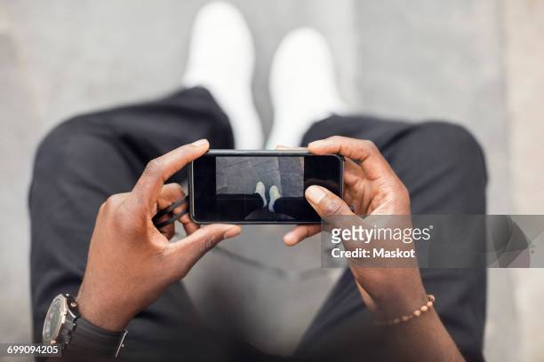 high angle view of man photographing legs on mobile phone - horizontal stock-fotos und bilder