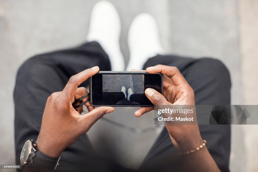 High angle view of man photographing legs on mobile phone