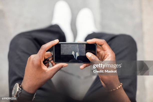 high angle view of man photographing legs on mobile phone - horizontaal stockfoto's en -beelden