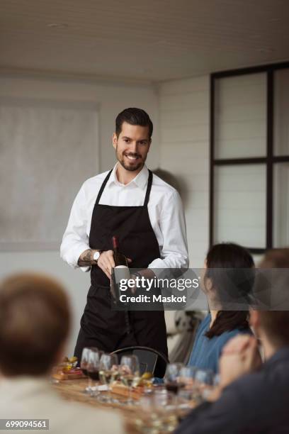 happy man showing wine bottle to business people at table - sommelier stockfoto's en -beelden