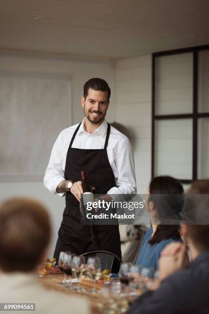happy man showing wine bottle to business people at table - sommelier stock pictures, royalty-free photos & images